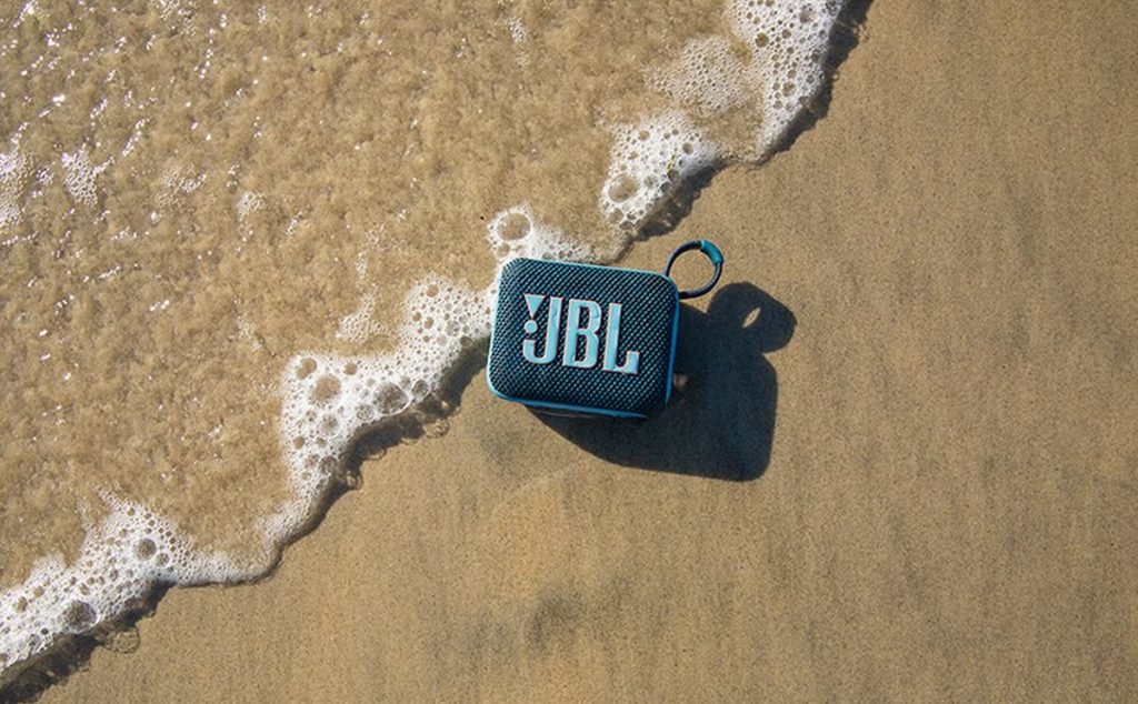 JBL Go 4 sur le sable d'une plage : une enceinte résistante à l'eau et à la poussière